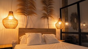 Un dormitorio con cabecera de madera, ropa de cama blanca y dos lámparas colgantes.
