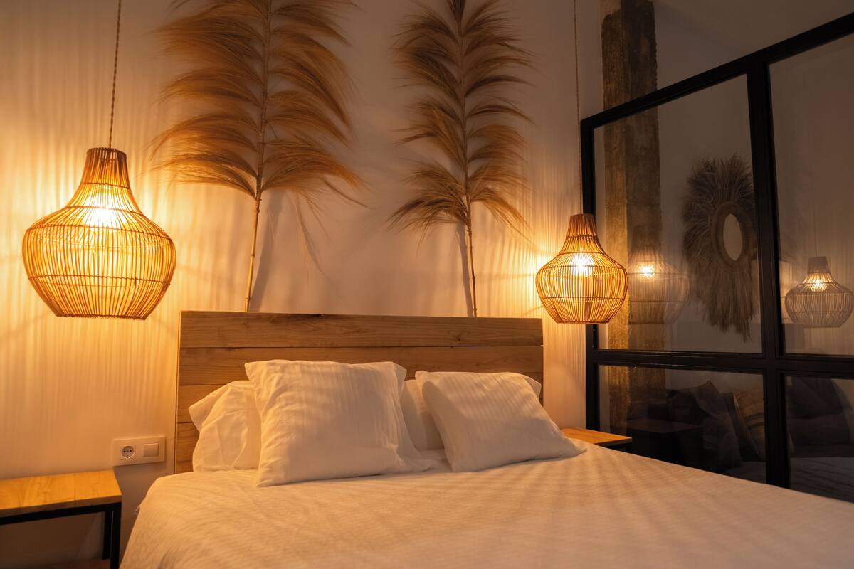 A bedroom with a wooden headboard, white bedding, and two hanging lamps.