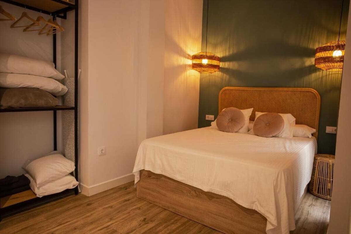 A neatly made bed with a wooden headboard, a shelf with folded towels, and two wall-mounted lamps.