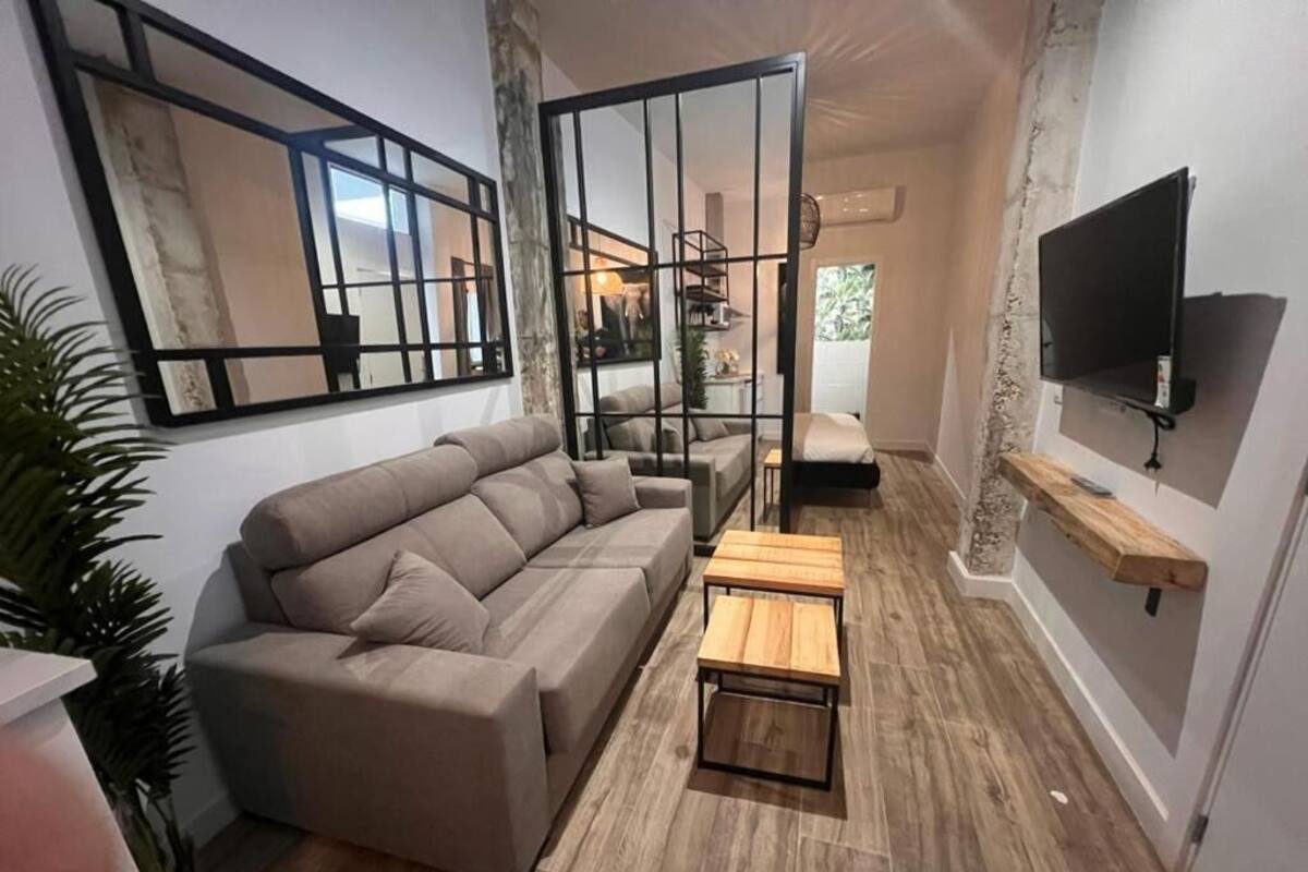 A living room with a sectional sofa, a wooden coffee table, a TV mounted on the wall, and a large mirror.