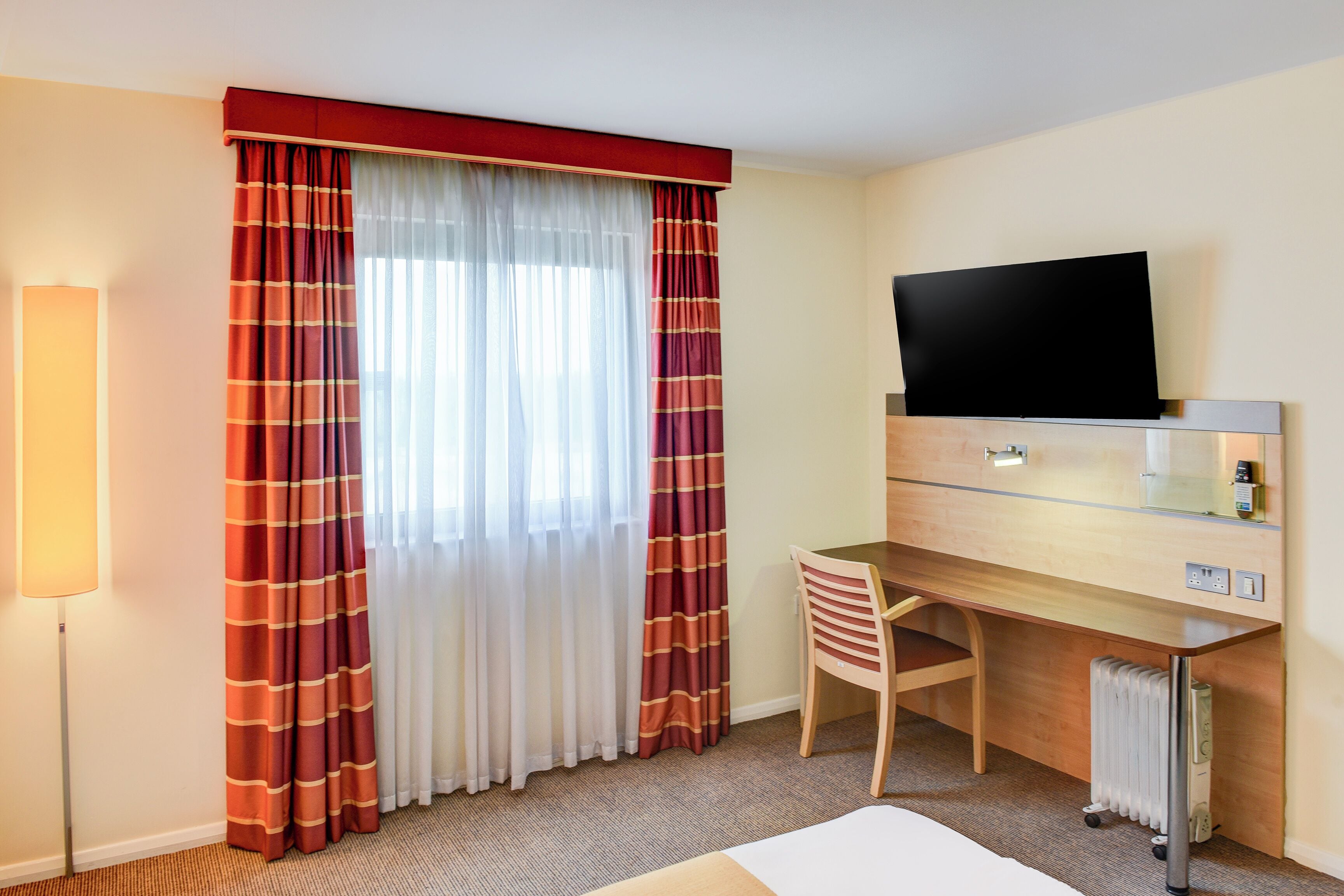 Una habitación de hotel con una cama, un escritorio, una silla, un televisor y un radiador.