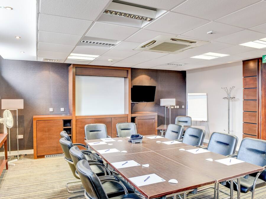 A conference room with a long table, multiple chairs, a projector screen, and a television.