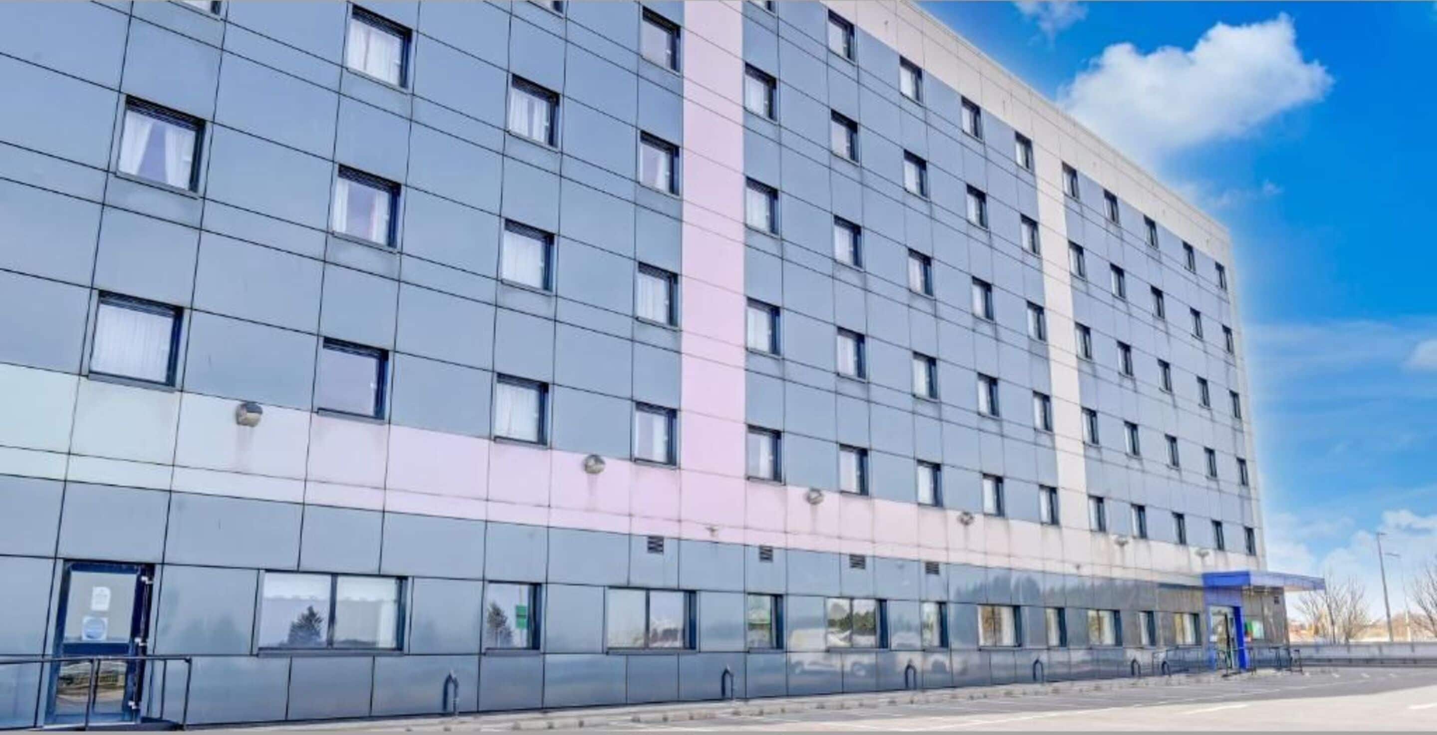 A modern hotel building with multiple floors, large windows, and EV charging stations available.