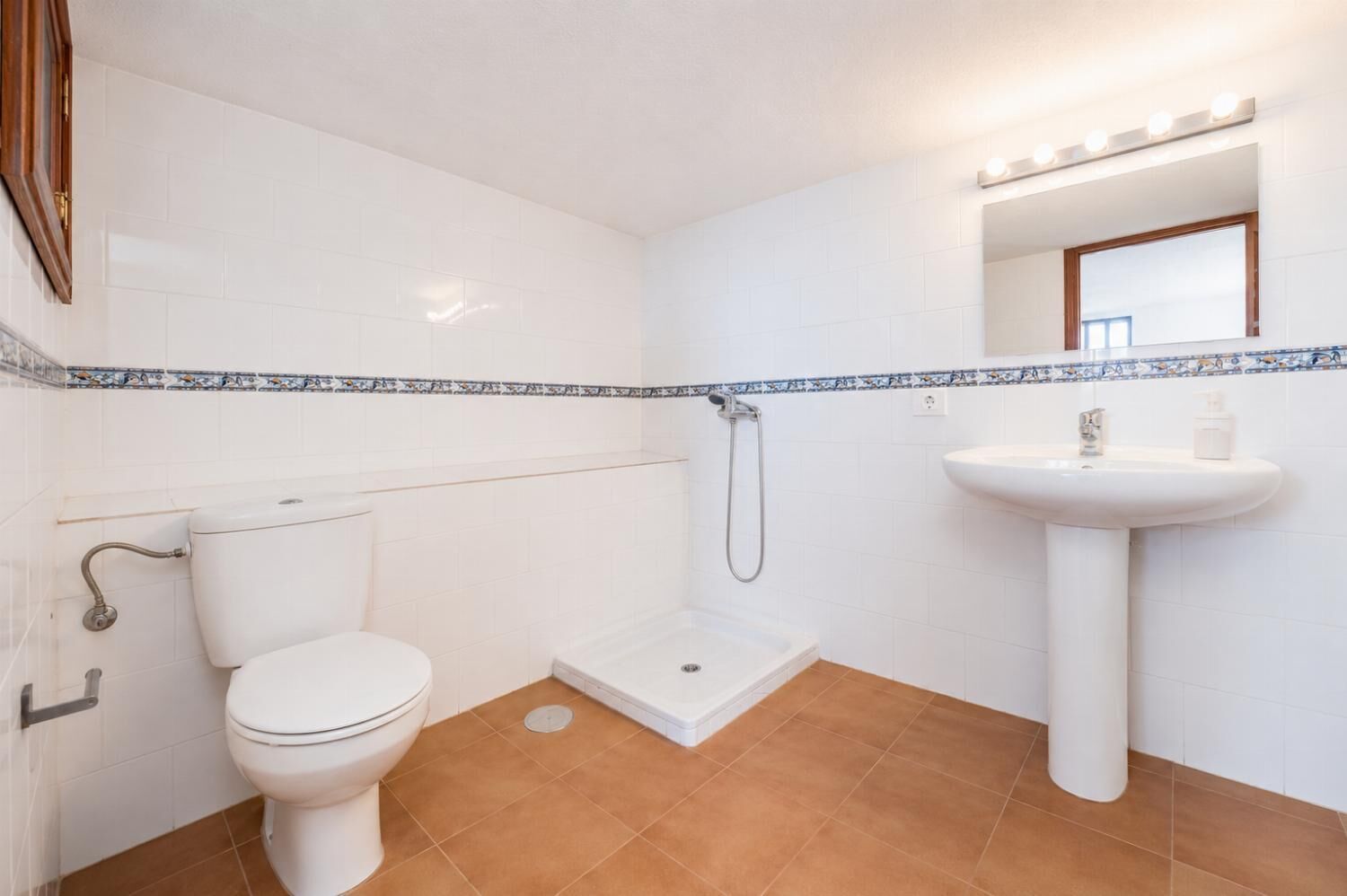 A bathroom with a toilet, shower, sink, and a mirror with lights.