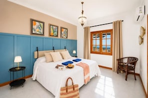 Une chambre à coucher comprenant un lit, une table de chevet, une chaise, une fenêtre avec des rideaux et des œuvres d’art accrochées au mur.