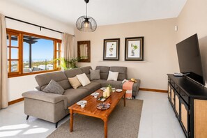 A living room with a sofa, coffee table, and TV. There are framed pictures on the wall and a window with curtains. - Villa Valiente - Four Bedroom Villa, Sleeps 8 (Tías)