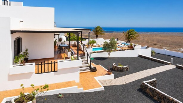 Un moderno edificio blanco con terraza en la azotea, mobiliario exterior, piscina y vista al mar.