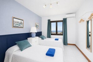 A hotel room with two beds, a nightstand, a lamp, a window with a view, and a mirror.