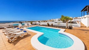 Una piscina en la azotea con tumbonas, una piscina pequeña circular y vista al mar.