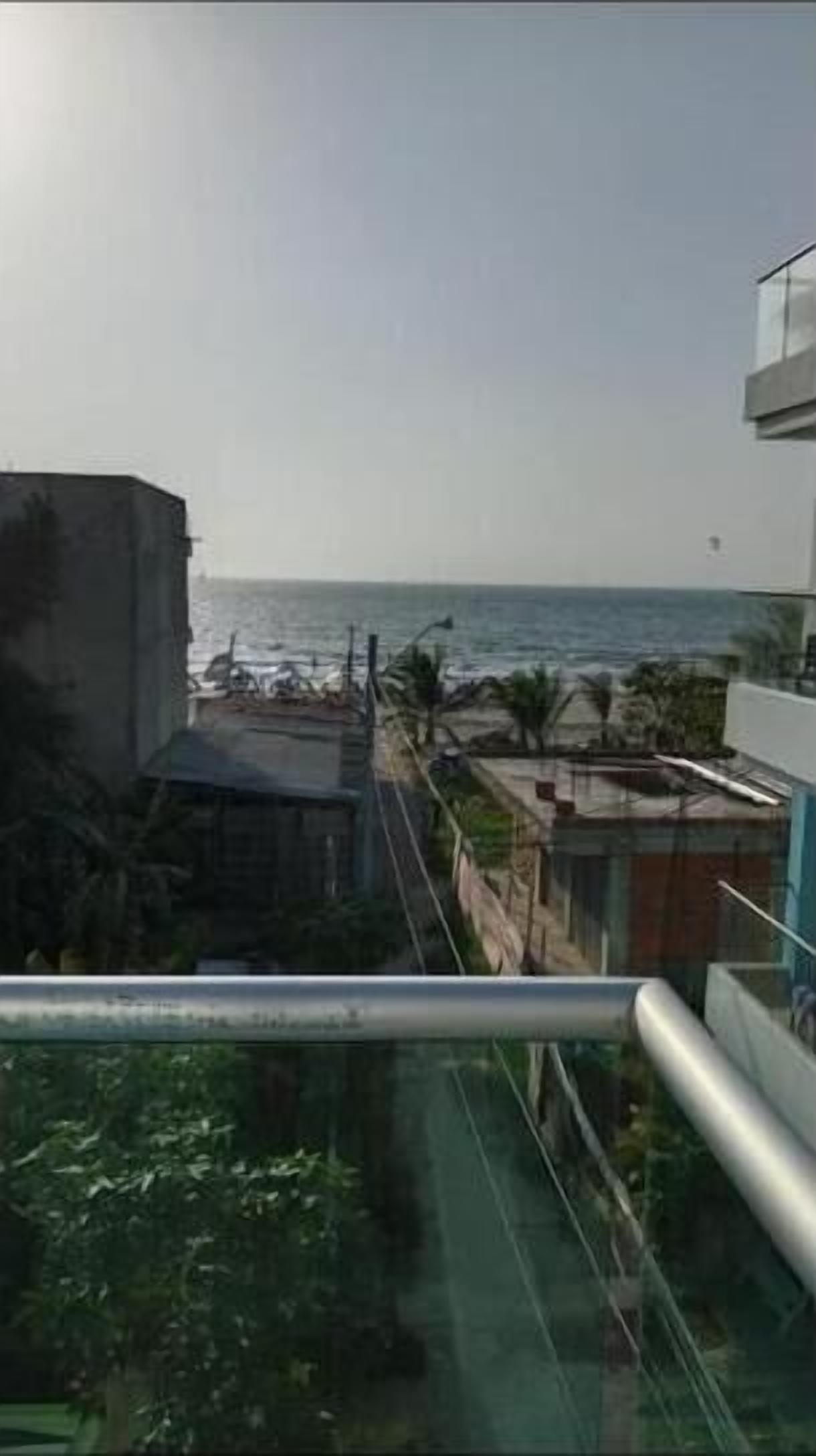 Vista desde un balcón sobre una zona costera con edificios, una playa y palmeras.