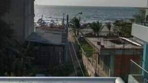 Vista de uma varanda com vista para a costa, com edifícios, praia e palmeiras.