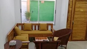 Um quarto com porta verde, sofá amarelo, cadeira de madeira e uma pequena mesa.