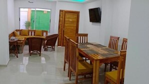 Uma área de refeições com uma mesa e cadeiras de madeira, uma porta verde e uma televisão na parede.