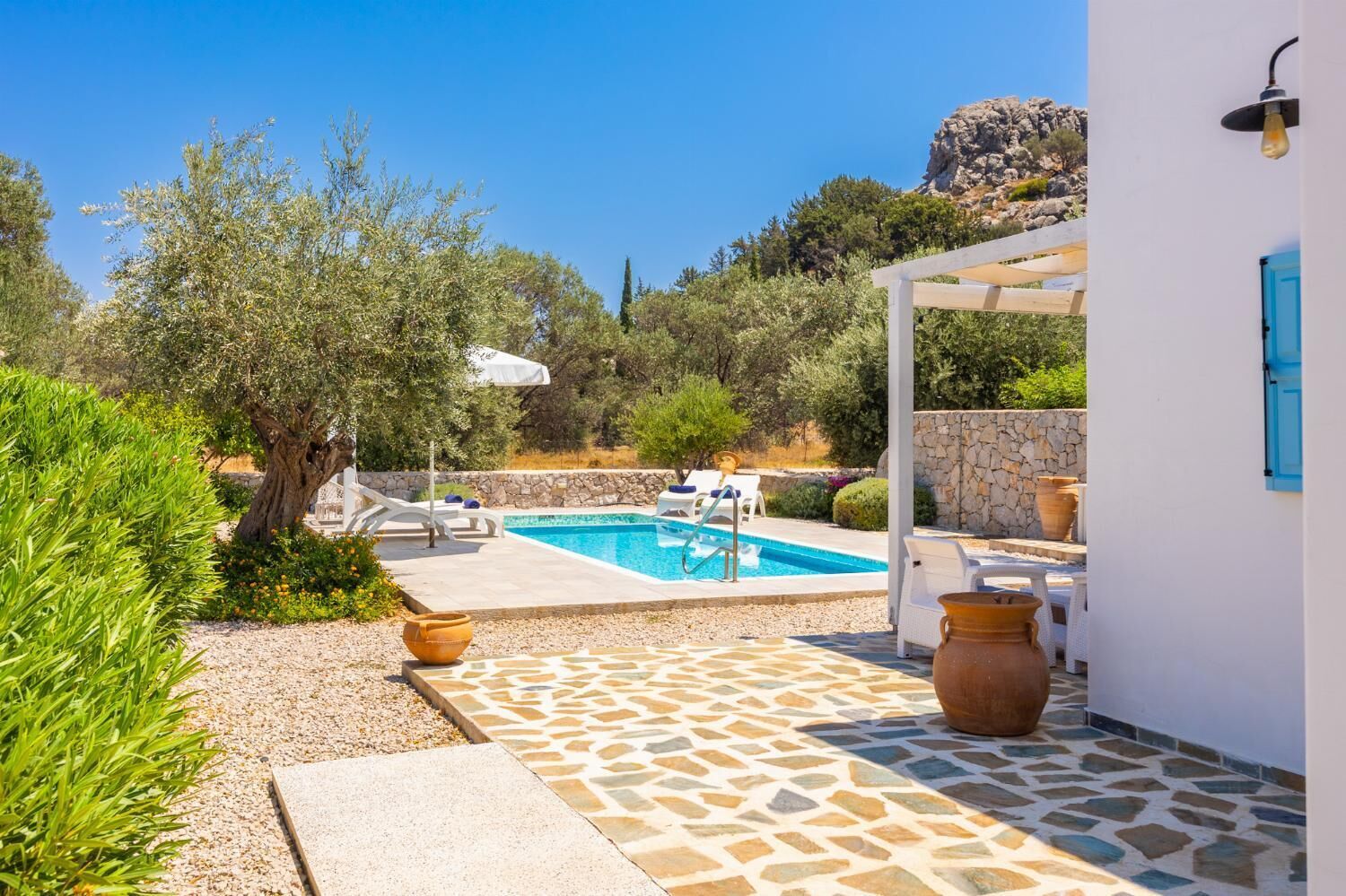 Un área de piscina con un deck de baldosas de piedra, sillas de descanso y una pérgola.