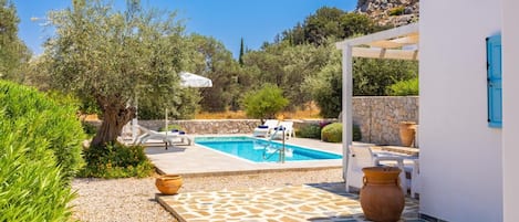 Un espace piscine doté d’une terrasse en pierre, de chaises longues et d’une pergola.