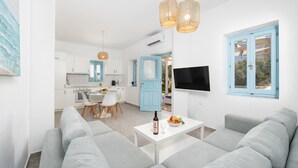 A modern living room with grey sofas, a white coffee table with a bottle and bowl, and a TV mounted on the wall.