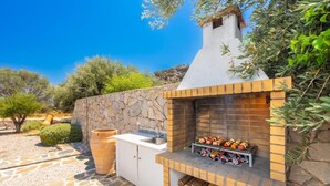 An outdoor kitchen with a stone wall, a sink, and a grill.