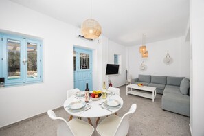 Un salon moderne avec un canapé gris, une table à manger dressée pour deux personnes et un téléviseur fixé au mur.