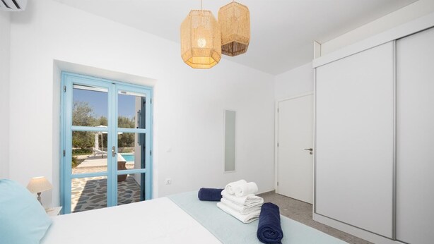 A bedroom with a bed, a blue door leading to a pool, and a wardrobe.