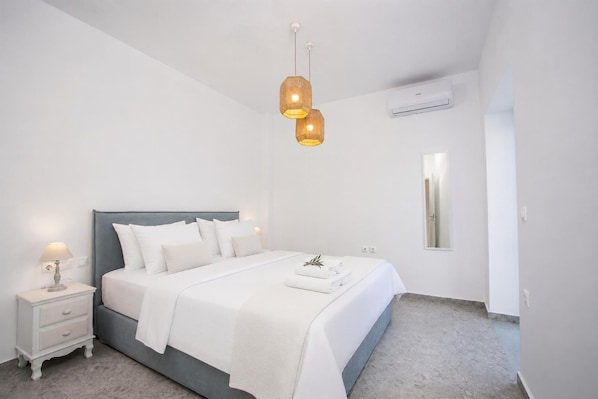 Een slaapkamer met een bed, nachtkastjes, een hanglamp, een airconditioner en een spiegel.