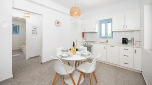 Una cocina moderna con armarios blancos, un comedor con mesa y sillas redondas, y una lámpara colgante.