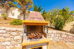 Ein Grill mit dem Markennamen 'PERMOZEL' auf der Vorderseite, umgeben von Steinmauern und viel Grün.