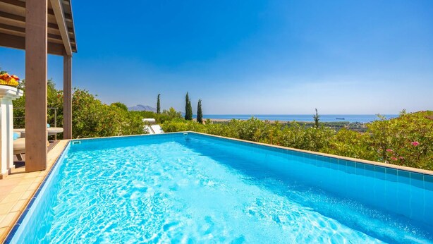 A rectangular swimming pool with clear blue water, surrounded by greenery and a view of the sea. - Villa Daphne - Two Bedroom Villa, Sleeps 4 (Kalathos)