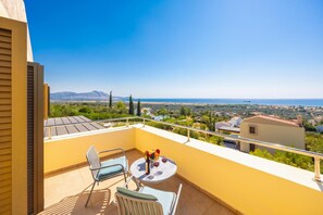 A balcony with a table, chairs, and a view of the sea and distant landscape.