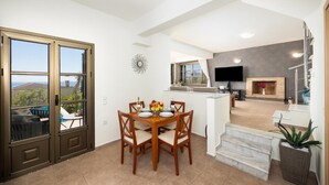 A dining area with a table set for four, a kitchen in the background, and a living area with a fireplace. - Villa Daphne - Two Bedroom Villa, Sleeps 4 (Kalathos)