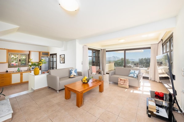 Una sala moderna con sofá, mesa de centro y comedor. Se observa una cocina con ventana y vistas al exterior.
