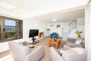 Una sala de estar moderna con televisor de pantalla plana, chimenea, una escalera y vistas al exterior.