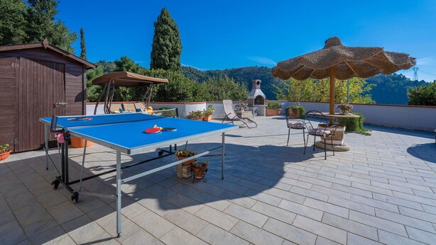 Mesa de ping pong, mobiliario exterior y zona de barbacoa en una azotea con vistas a colinas.