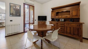Un comedor con una mesa redonda, sillas blancas, un mueble de madera con un televisor y un radiador.