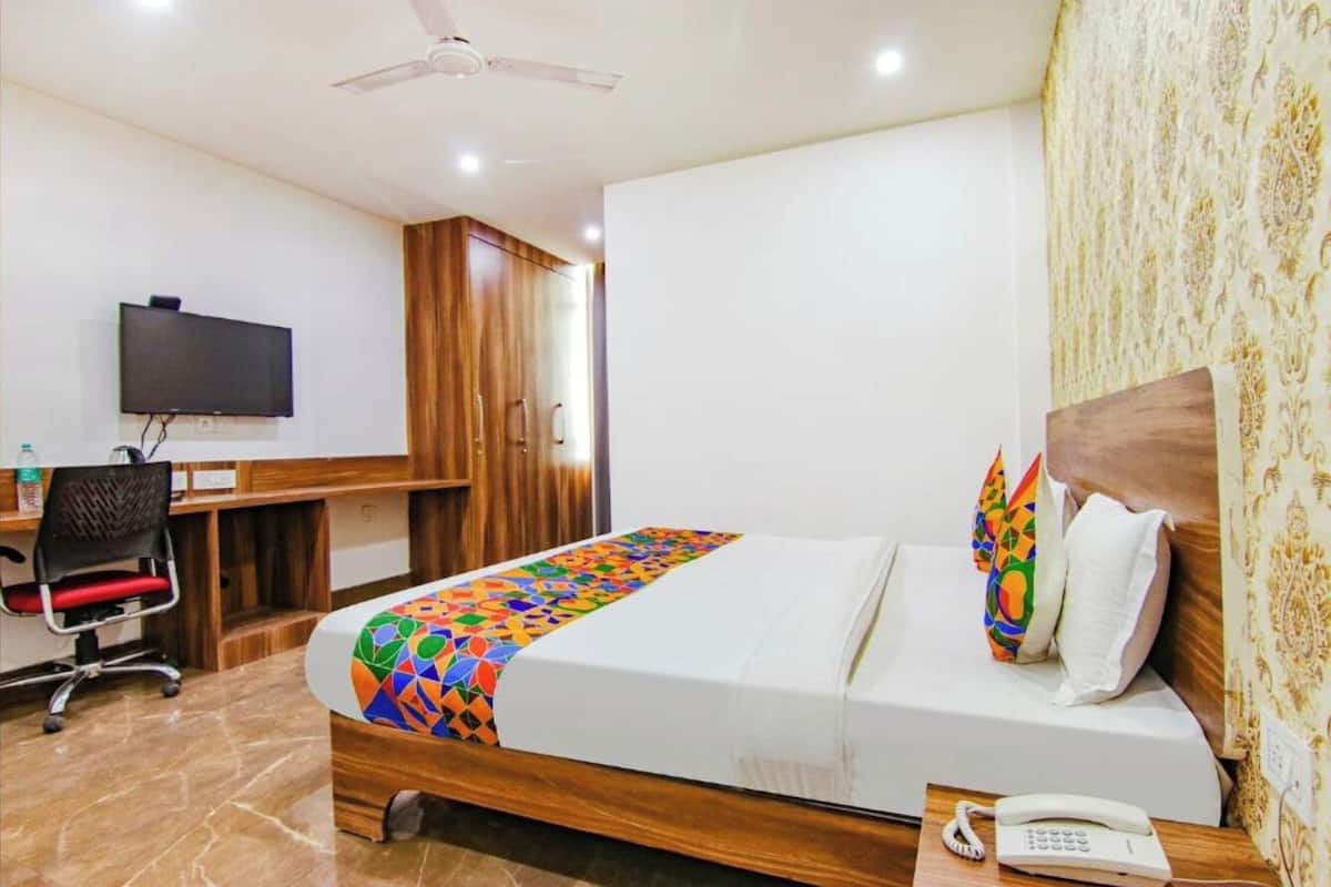 A hotel room with a bed, a desk, a chair, a telephone, and a television.