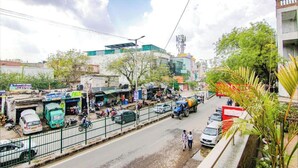 A busy street scene with shops, parked cars, and a few pedestrians. - Hotel Divine Residency by JMD Group (New Delhi)