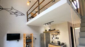 A modern loft apartment with a loft bed, a kitchen area, a dining table, and a large TV. - LOFT Mar 101 - Private Pool - Just Steps from Gastronomic Villages (Tatuamunha)
