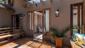 A wooden deck with a bench, a potted plant, and a view into the house. - Residência Flora (Porto Seguro)