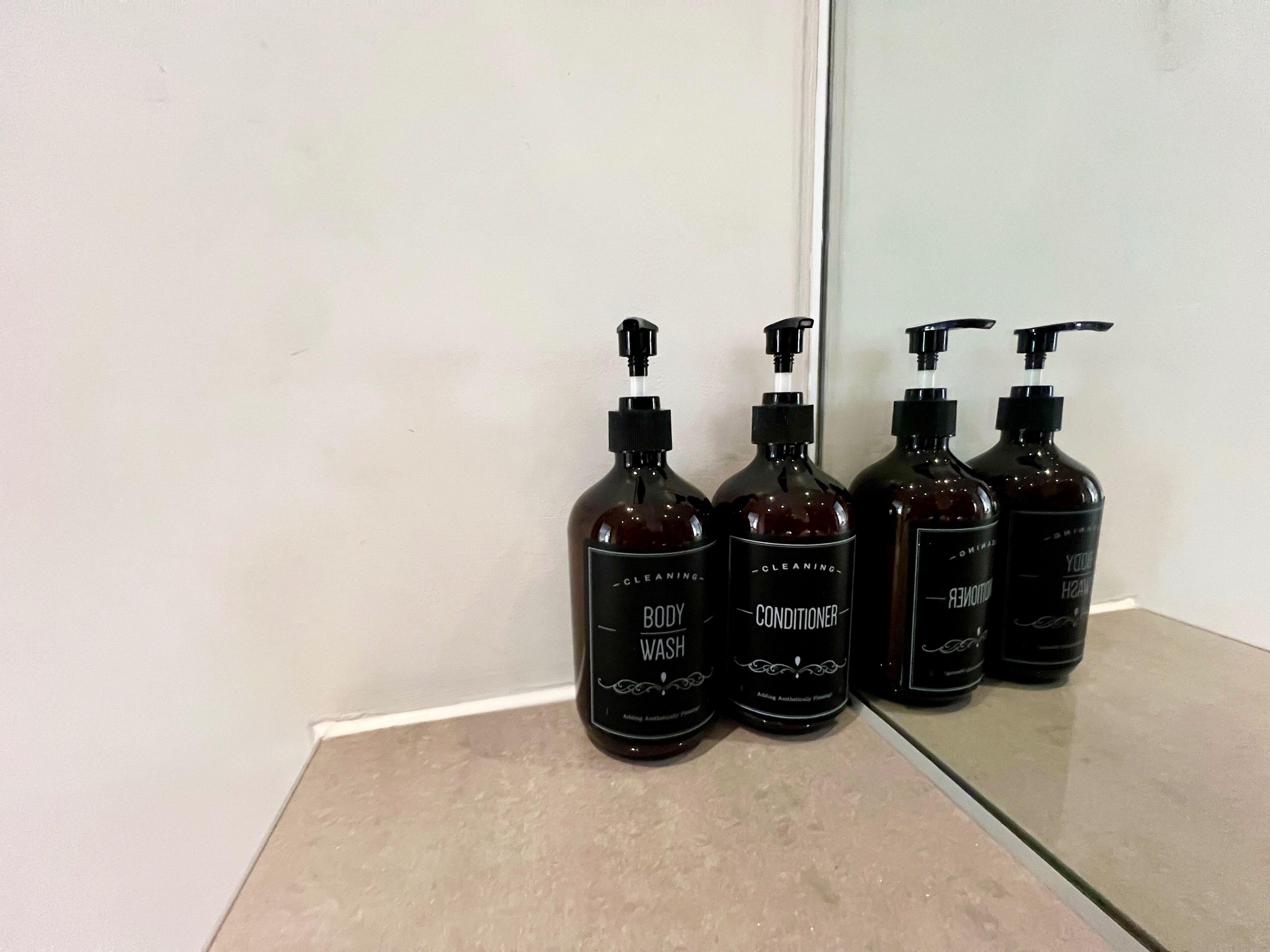 Quatre bouteilles de gel douche et d’après-shampoing sont posées sur un comptoir.