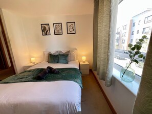 Een net opgemaakt bed met een groene deken, twee bedlampen en drie ingelijste kunstwerken aan de muur.