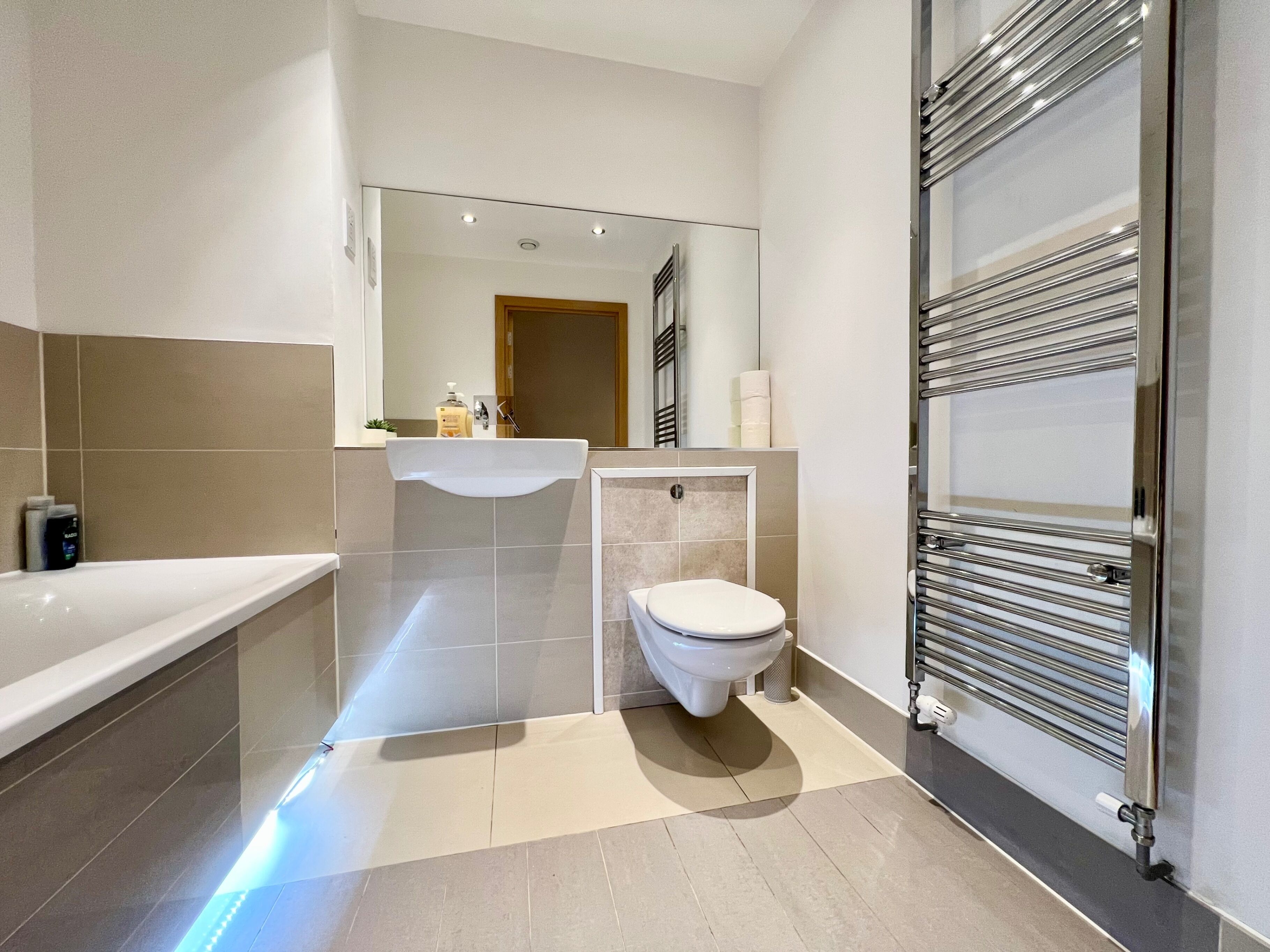 A modern bathroom with a bathtub, toilet, and a large mirror.