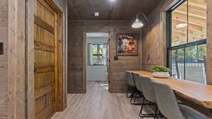 A wooden interior with a long table and chairs, a door, and a window with a view. - Ozark Shores- Lakefront, Hot Tub, Air Hockey (Shirley)