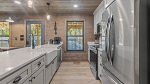 A modern kitchen with wooden ceiling, stainless steel appliances, and a large window. - Ozark Shores- Lakefront, Hot Tub, Air Hockey (Shirley)