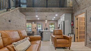 A spacious living area with a leather sofa, a leather armchair, and a central island with a kitchen in the background. - Ozark Shores- Lakefront, Hot Tub, Air Hockey (Shirley)