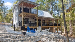 A two-story cabin with a balcony, surrounded by trees and featuring outdoor seating. - Ozark Shores- Lakefront, Hot Tub, Air Hockey (Shirley)