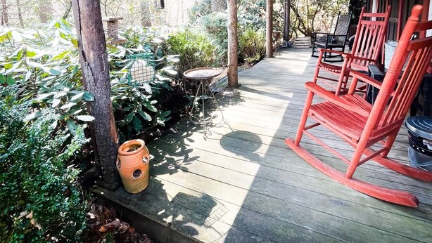 Eine Holzterrasse mit roten Schaukelstühlen, einem kleinen Tisch und Topfpflanzen.