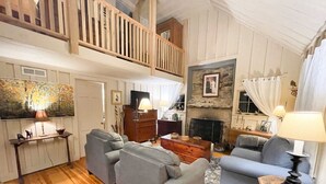 Ein geräumiges Wohnzimmer mit Holzboden, Kamin und einem Balkon mit Holzgeländer.