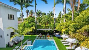 A swimming pool with a sun deck, lounge chairs, and a covered seating area surrounded by palm trees and greenery. - Villa Tortuga: 10 BR 9,500 sq. ft Extravagant Miami Estate w pool, movie theater (Miami)