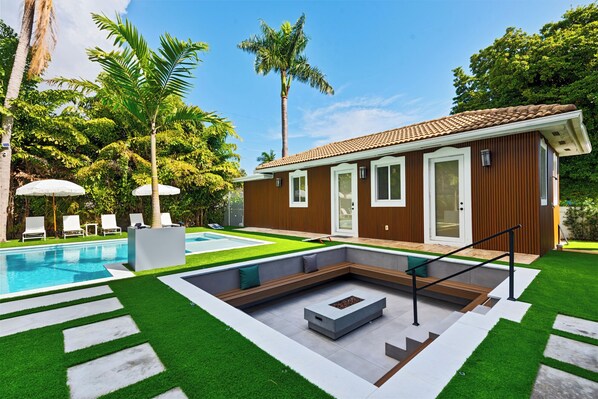 Una casa moderna con piscina, una pequeña terraza y exuberante follaje.