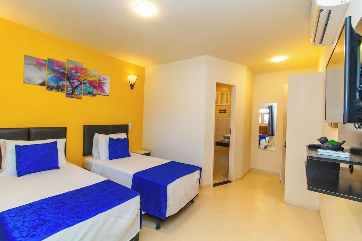 A hotel room with two beds, a kitchenette, and a bathroom visible through an open door.