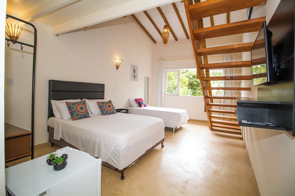 A bedroom with two beds, a TV, a desk, and a staircase.